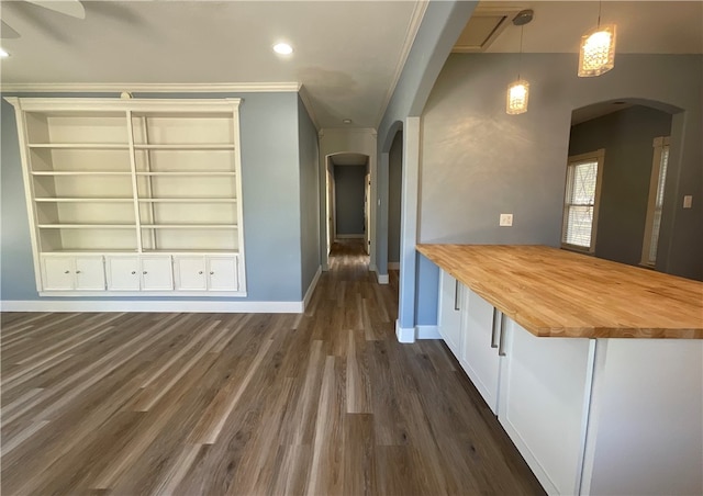 interior space featuring baseboards, dark wood finished floors, a peninsula, arched walkways, and wood counters