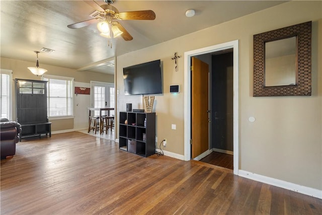 living area with a ceiling fan, visible vents, baseboards, and wood finished floors