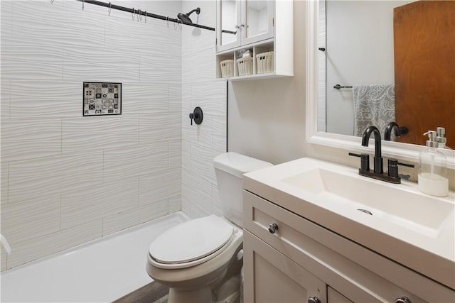 bathroom featuring toilet, a tile shower, and vanity