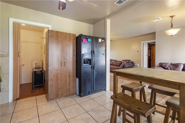 kitchen featuring light tile patterned flooring, black fridge with ice dispenser, and visible vents