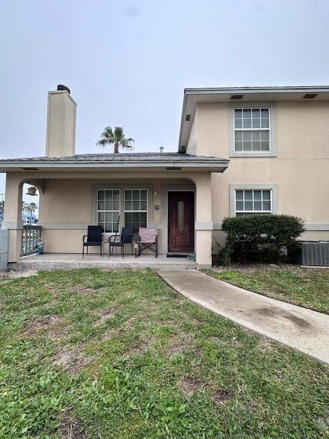 view of front of home with a chimney, central AC unit, a front lawn, and stucco siding