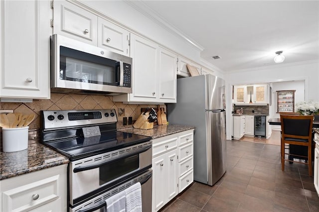 kitchen featuring dark stone counters, white cabinets, decorative backsplash, ornamental molding, and stainless steel appliances