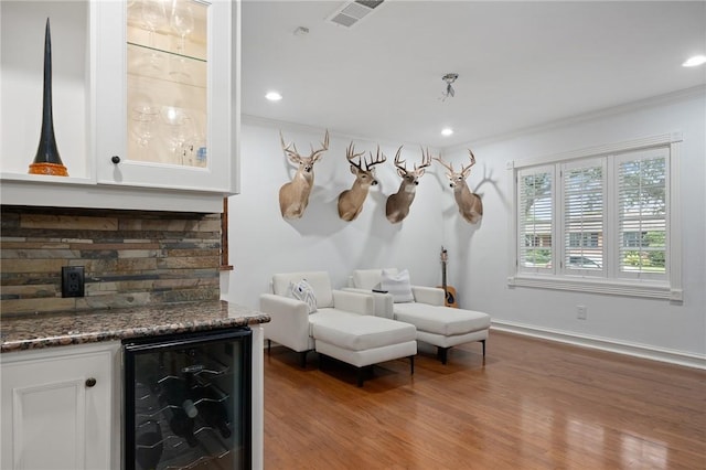 living area with bar area, crown molding, beverage cooler, and wood-type flooring