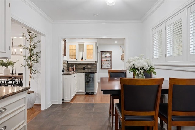 dining area featuring dark tile patterned floors, an inviting chandelier, beverage cooler, and crown molding