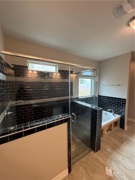 bathroom with a bath, a wealth of natural light, a shower stall, and visible vents