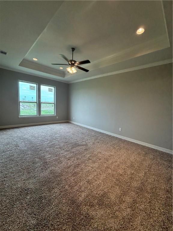 carpeted empty room featuring a tray ceiling, crown molding, baseboards, and ceiling fan