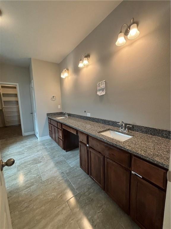 bathroom with a walk in closet, a sink, baseboards, and double vanity