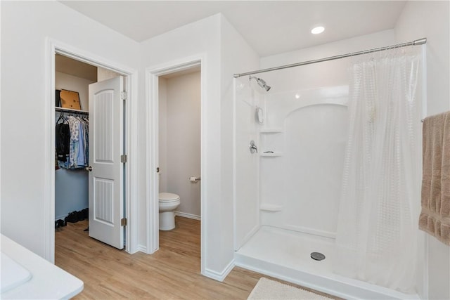 full bathroom featuring toilet, wood finished floors, baseboards, a stall shower, and a walk in closet