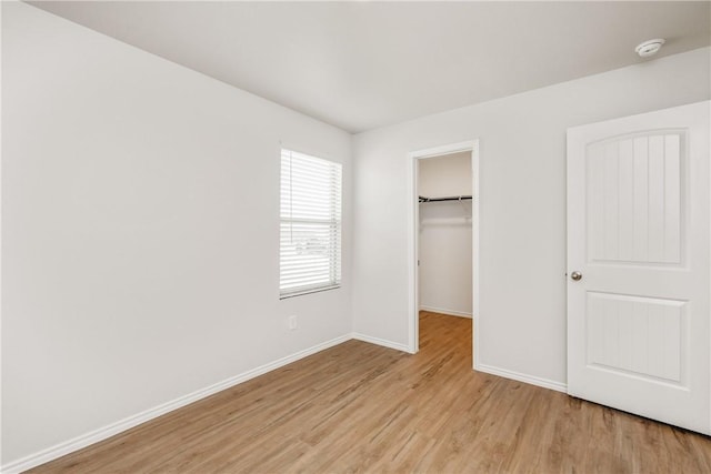 unfurnished bedroom with baseboards, a closet, a walk in closet, and light wood-style floors