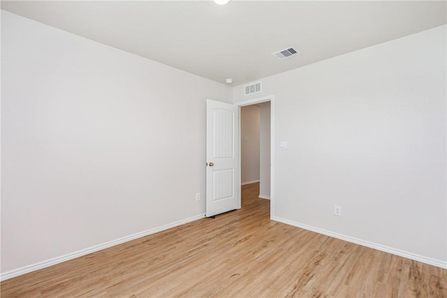 empty room with light wood-style floors, visible vents, and baseboards