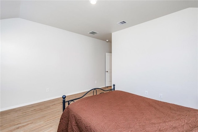 bedroom featuring light wood-style floors, visible vents, and vaulted ceiling