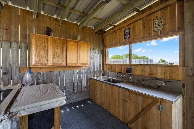 kitchen with brown cabinetry, a sink, carpet, and wood walls