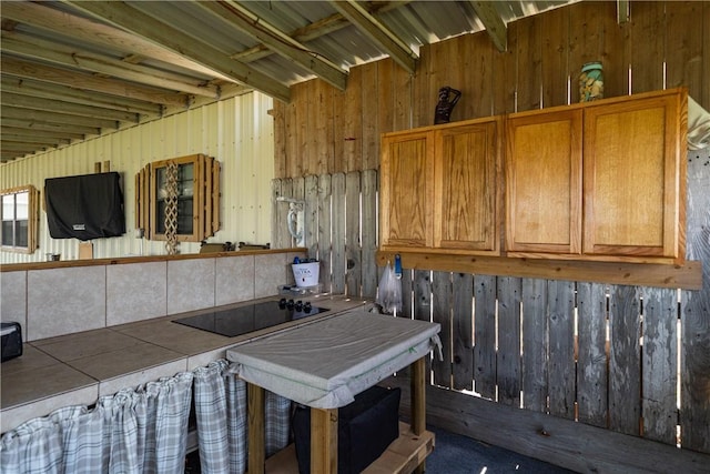 kitchen featuring wooden walls, tile countertops, brown cabinets, and black electric cooktop