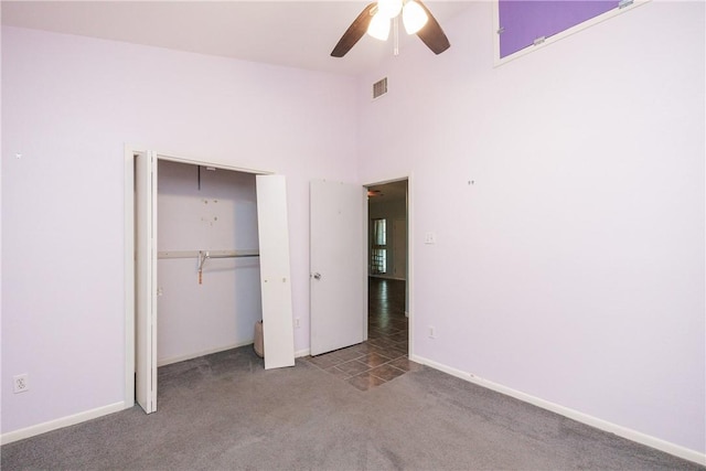 unfurnished bedroom with ceiling fan, carpet flooring, a closet, and a high ceiling