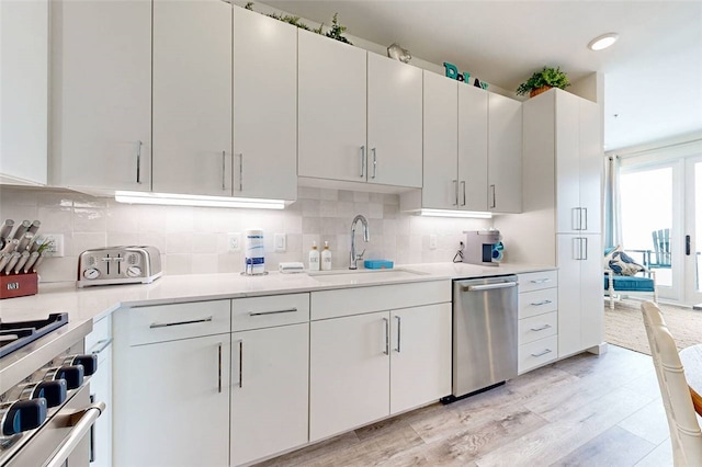 kitchen featuring white cabinets, decorative backsplash, dishwasher, sink, and light wood-type flooring