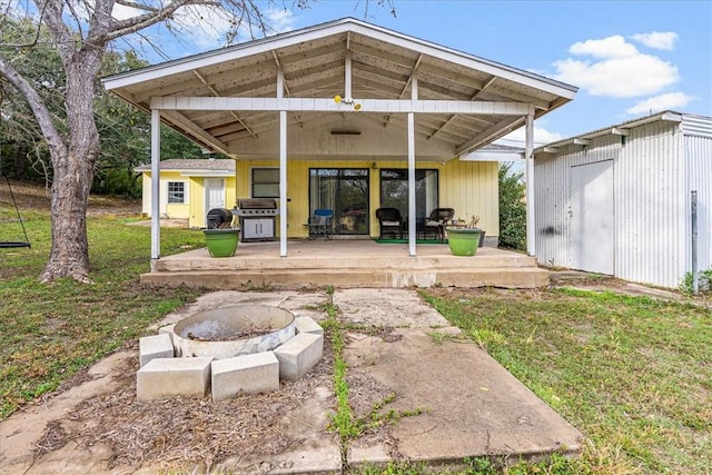 rear view of property with an outdoor structure, a lawn, a patio, and a fire pit