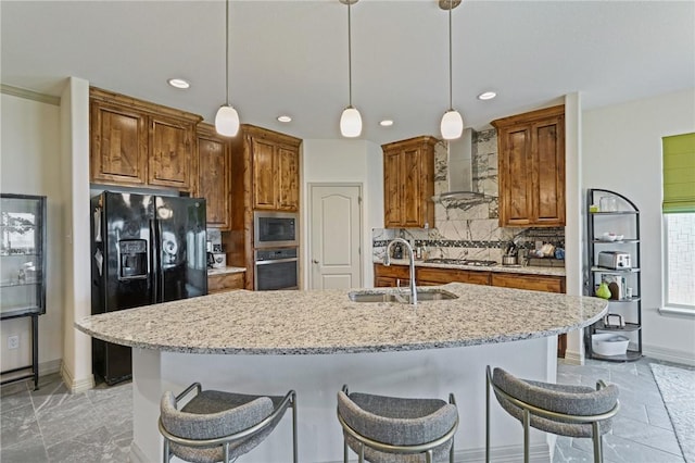 kitchen with stainless steel appliances, hanging light fixtures, a center island with sink, and wall chimney exhaust hood