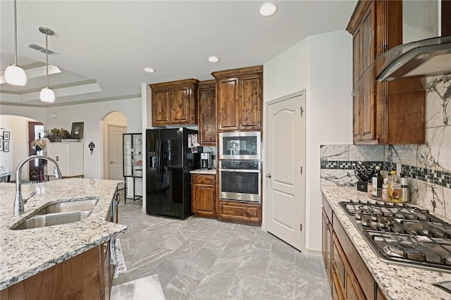 kitchen with sink, hanging light fixtures, light stone counters, stainless steel appliances, and wall chimney exhaust hood