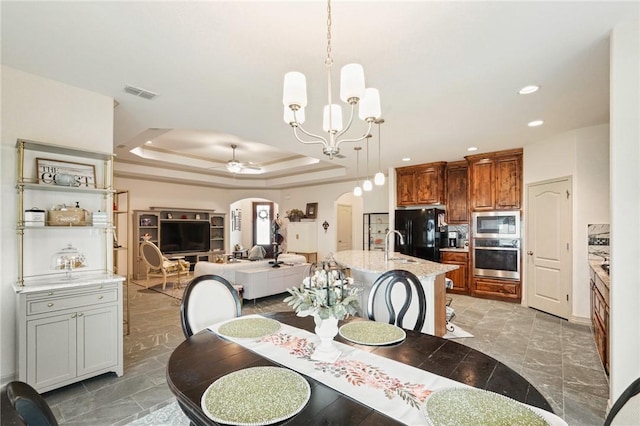 dining area with a raised ceiling, sink, and ceiling fan with notable chandelier