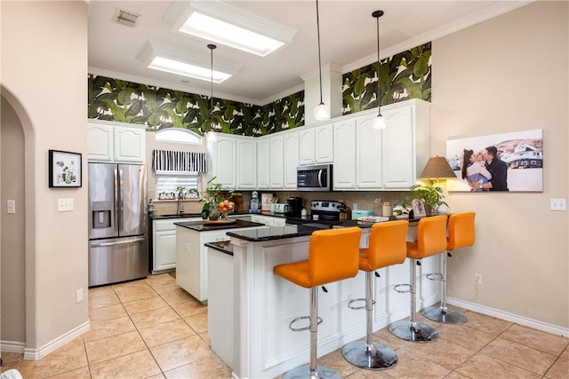 kitchen with white cabinets, appliances with stainless steel finishes, a kitchen bar, and kitchen peninsula