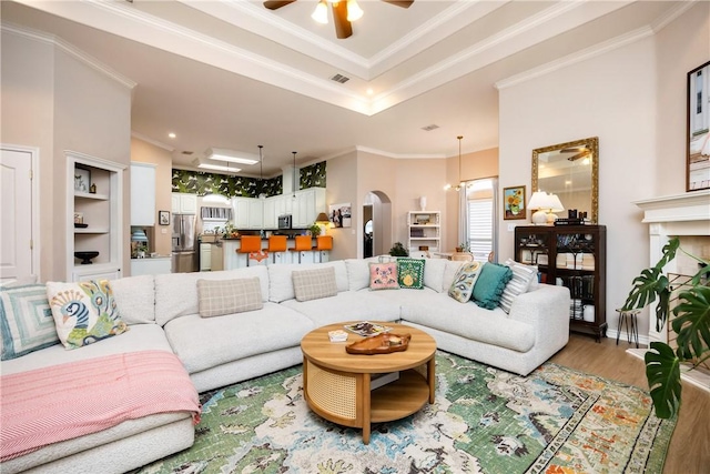 living room featuring ceiling fan, a fireplace, wood-type flooring, and ornamental molding