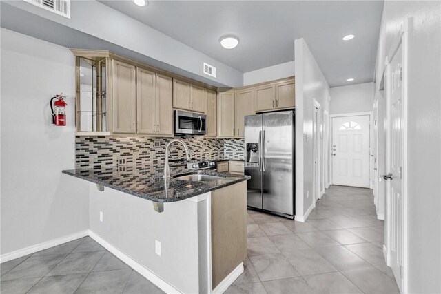 kitchen featuring decorative backsplash, dark stone countertops, a peninsula, and stainless steel appliances