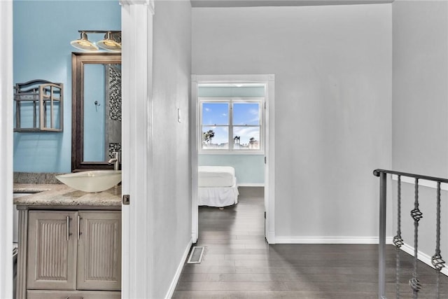 corridor featuring a sink, visible vents, baseboards, and wood finished floors