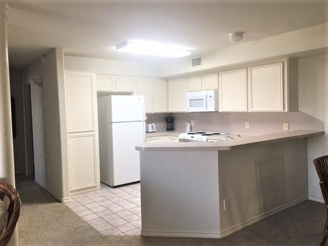 kitchen featuring kitchen peninsula, white appliances, light tile patterned floors, and white cabinets