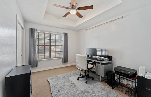 office featuring carpet floors, a tray ceiling, ceiling fan, and baseboards