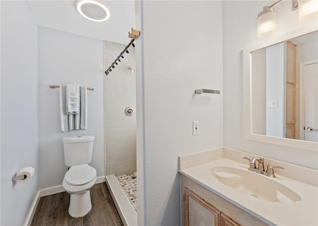 bathroom with baseboards, toilet, wood finished floors, a tile shower, and vanity