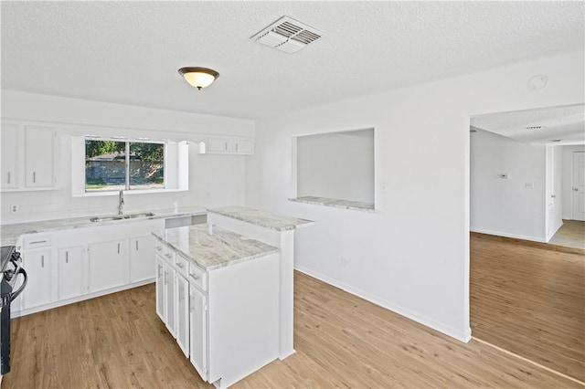 kitchen featuring white cabinets, light stone countertops, light hardwood / wood-style floors, and a kitchen island