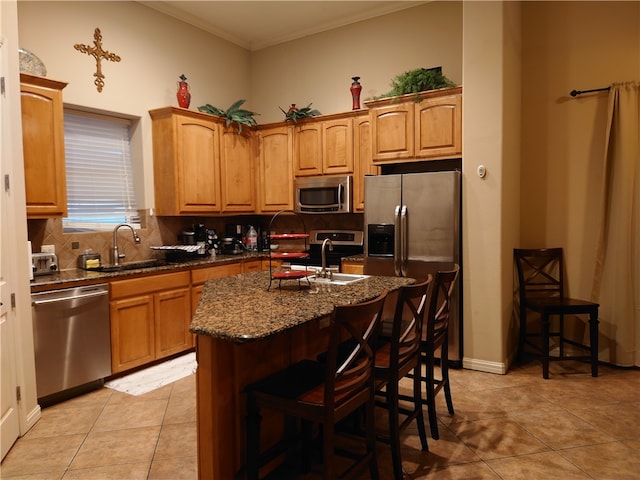 kitchen with appliances with stainless steel finishes, a kitchen bar, sink, decorative backsplash, and an island with sink