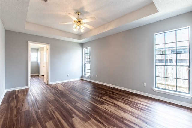 spare room with dark wood-style floors, a tray ceiling, a textured ceiling, and baseboards