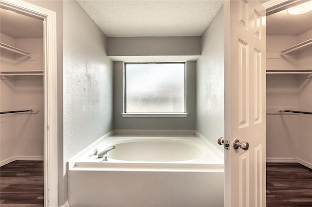 full bathroom featuring a textured ceiling, a textured wall, wood finished floors, and a bath