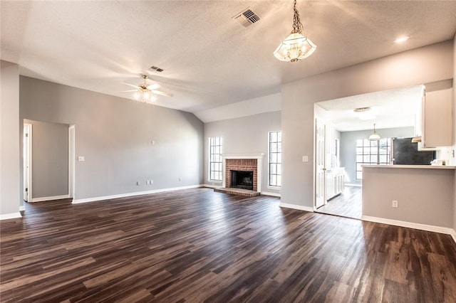 unfurnished living room with lofted ceiling, dark wood-style flooring, a fireplace, visible vents, and a ceiling fan