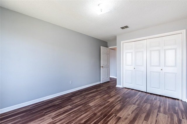 unfurnished bedroom with a textured ceiling, dark wood-style flooring, visible vents, baseboards, and a closet