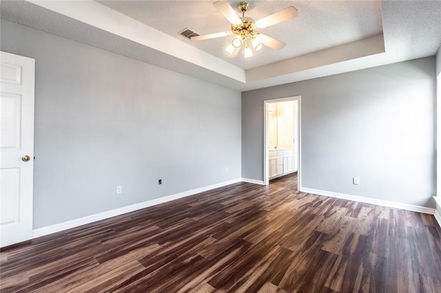 spare room featuring dark wood-style floors, a raised ceiling, visible vents, and baseboards