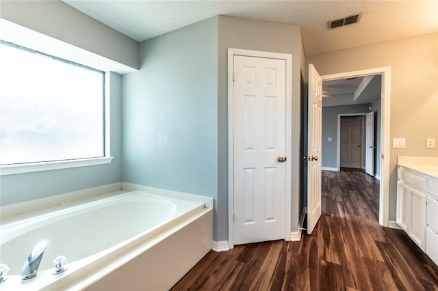 bathroom with baseboards, visible vents, wood finished floors, a garden tub, and vanity