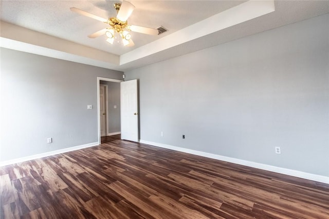 spare room with ceiling fan, visible vents, baseboards, dark wood-style floors, and a raised ceiling