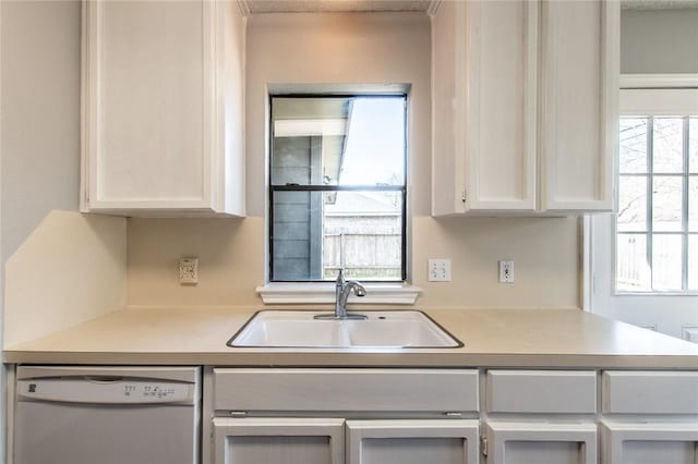 kitchen with white dishwasher, white cabinets, a sink, and light countertops