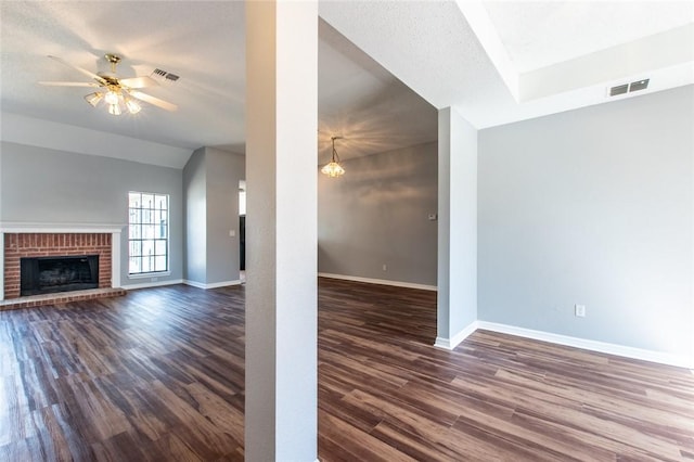 unfurnished living room with dark wood-type flooring, a brick fireplace, visible vents, and baseboards