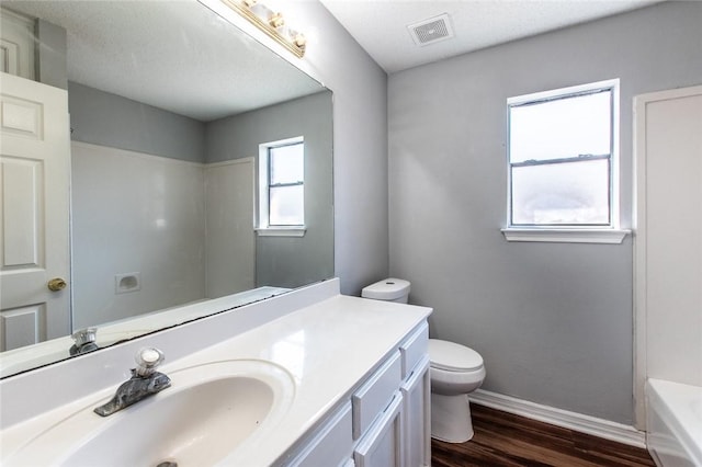 full bathroom with a washtub, visible vents, toilet, wood finished floors, and baseboards