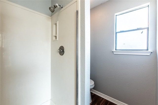 bathroom featuring toilet, baseboards, walk in shower, and wood finished floors