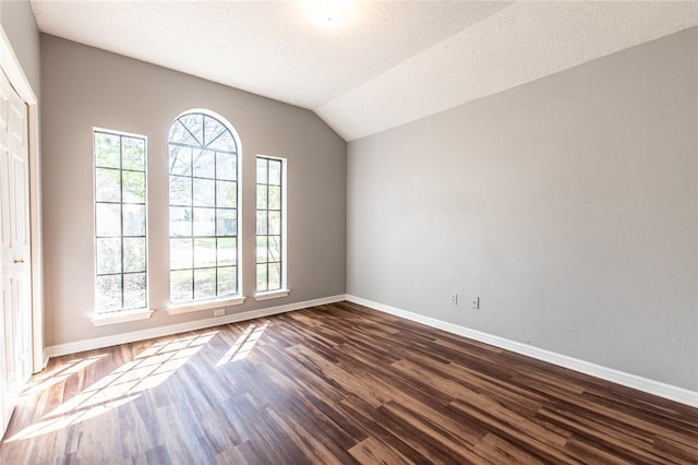 empty room with lofted ceiling, dark wood-style flooring, a textured ceiling, and baseboards