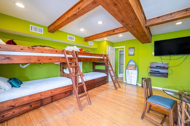 bedroom with beam ceiling, visible vents, baseboards, and wood finished floors