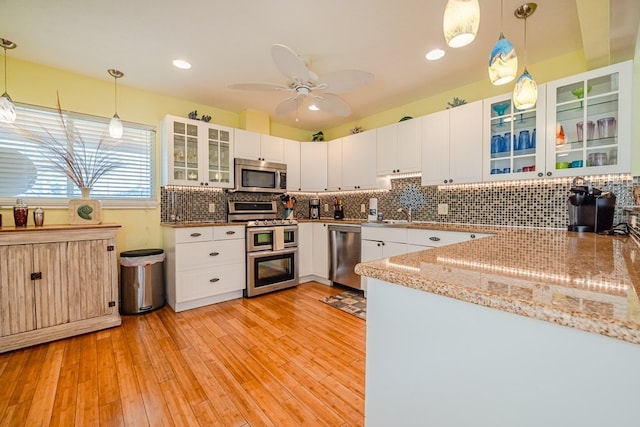 kitchen featuring stainless steel appliances, hanging light fixtures, decorative backsplash, light wood-style floors, and white cabinetry