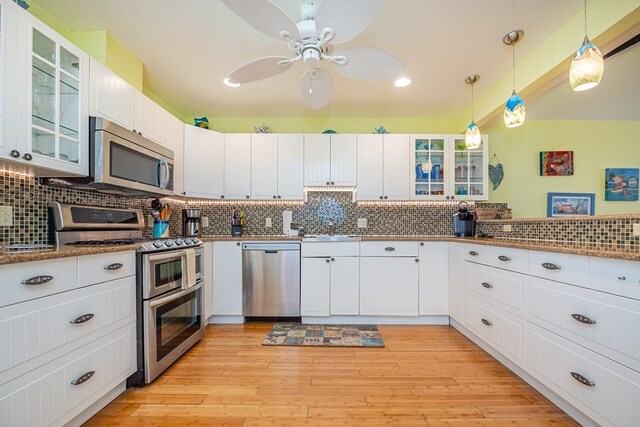 kitchen with decorative backsplash, appliances with stainless steel finishes, white cabinets, a sink, and light wood-type flooring