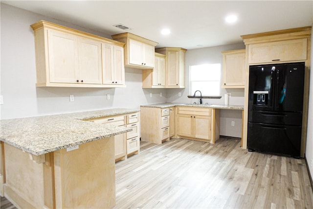 kitchen with black refrigerator with ice dispenser, light stone counters, sink, light hardwood / wood-style floors, and kitchen peninsula