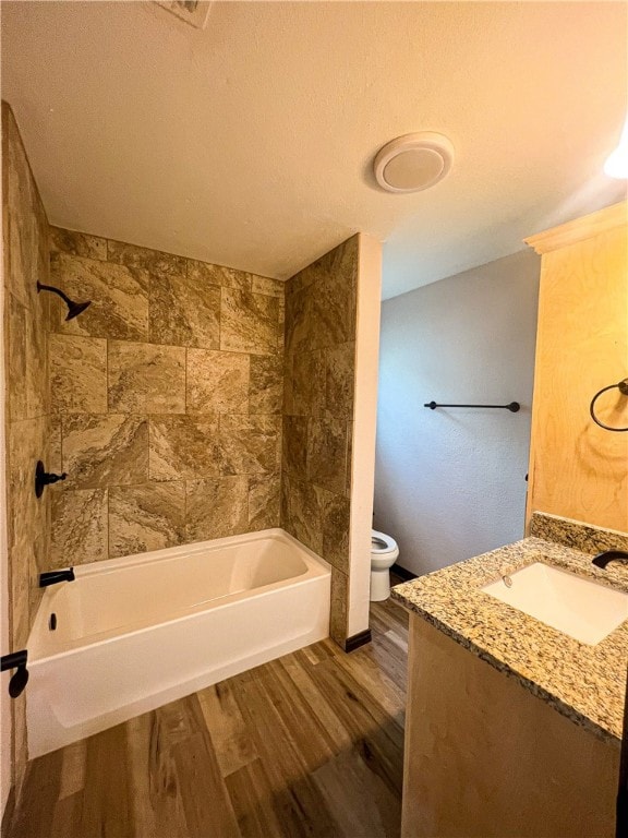 full bathroom with vanity, a textured ceiling, hardwood / wood-style flooring, toilet, and tiled shower / bath