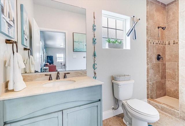 bathroom with vanity, toilet, tiled shower, and a wealth of natural light